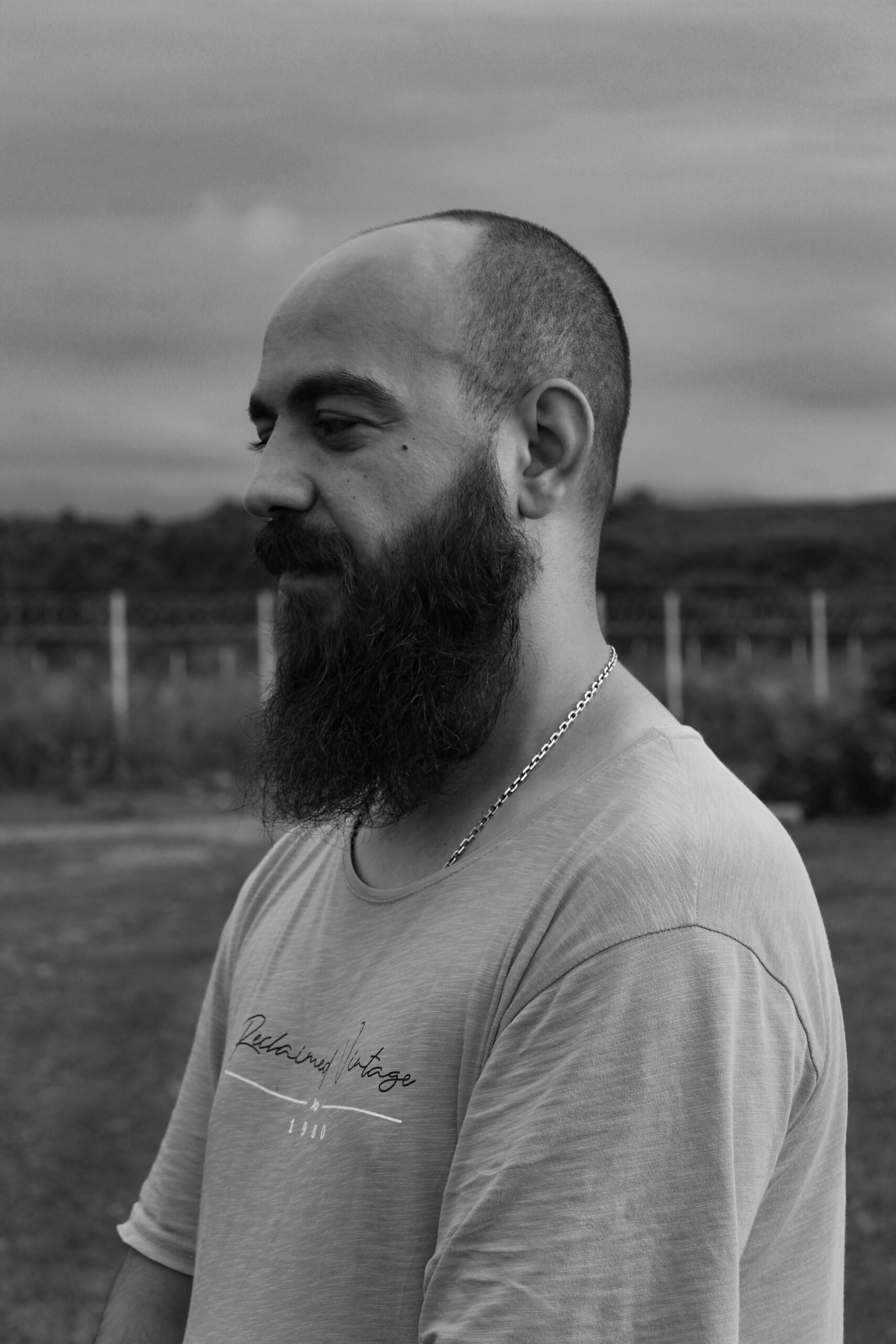 Black and white portrait of a bearded man outdoors, exuding a reflective mood.