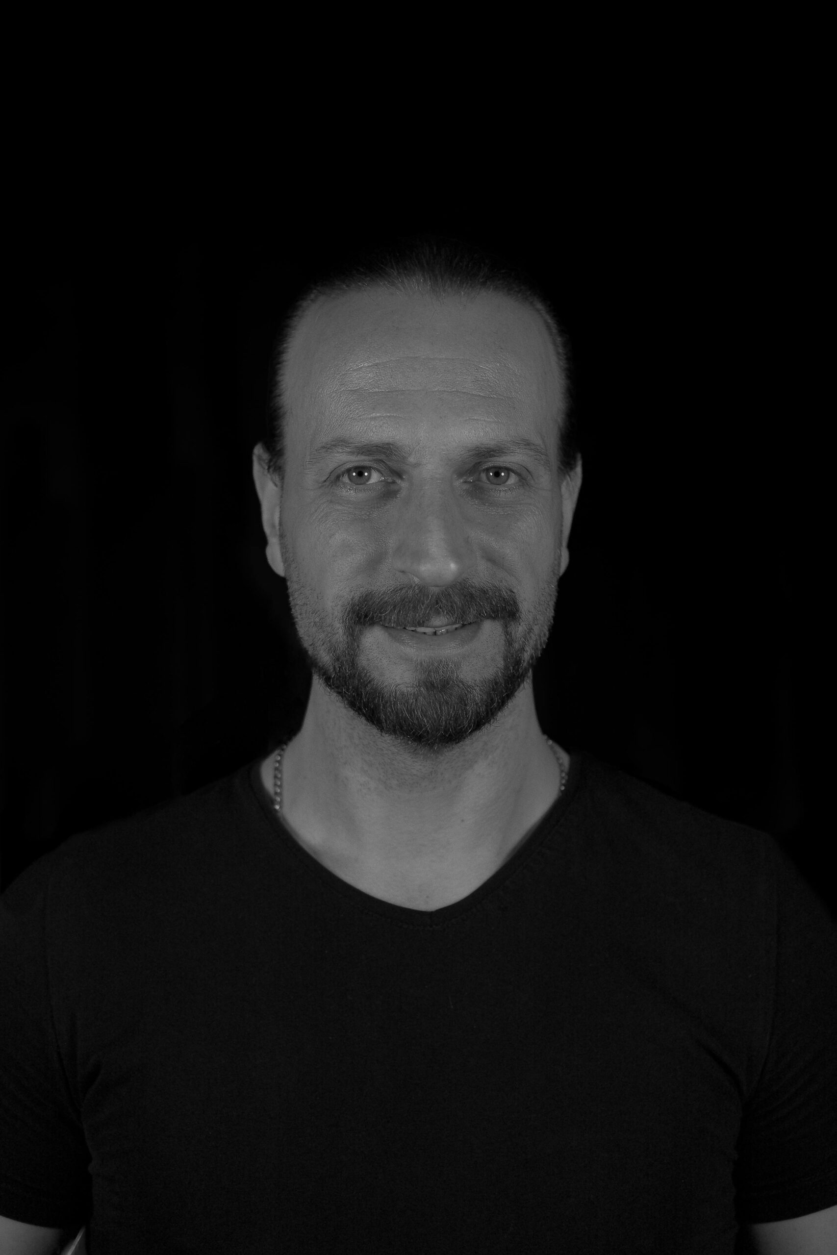 Black and white portrait of a smiling man with a beard against a dark background.