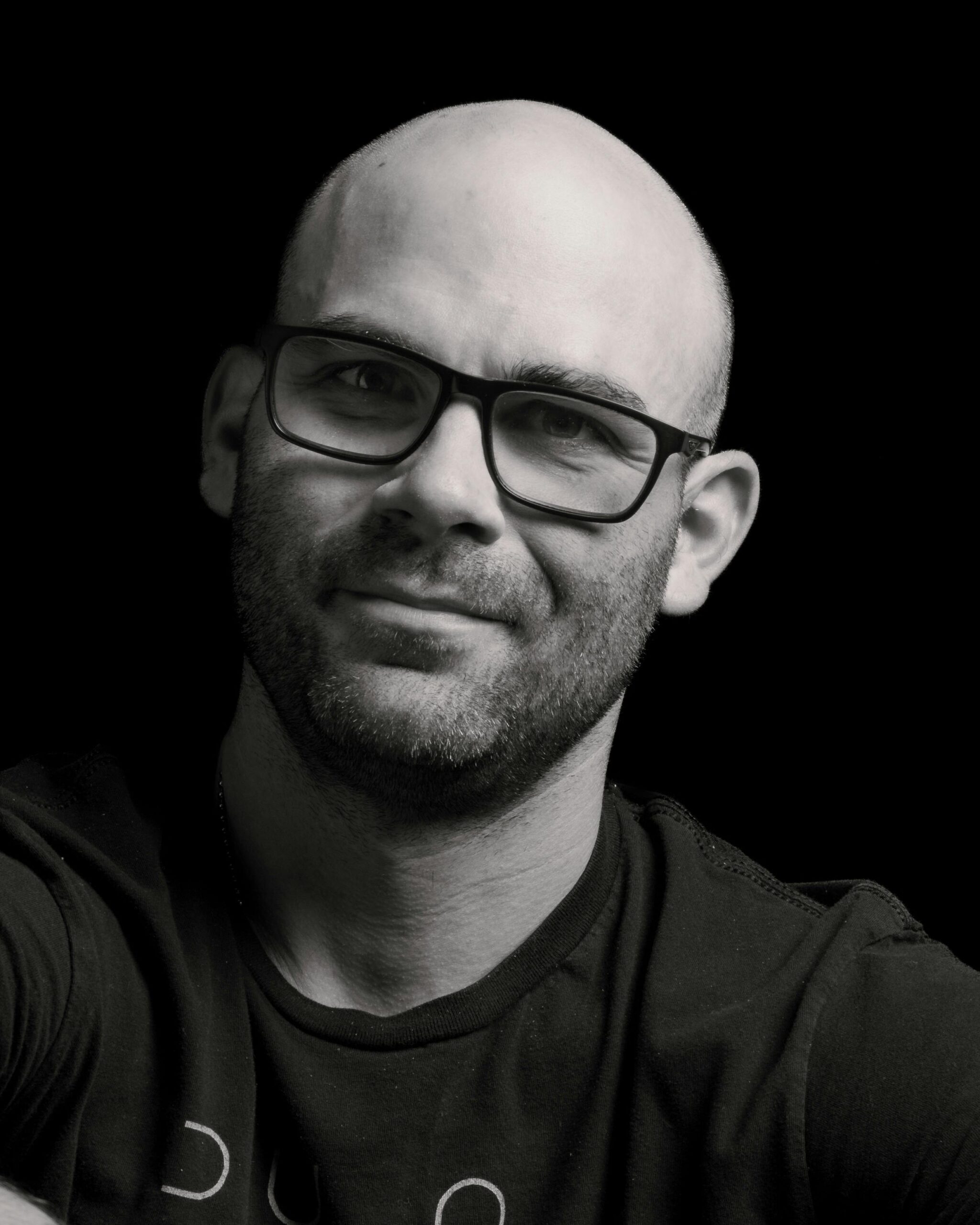 Monochrome portrait of a smiling bald man with glasses, showing a friendly expression.